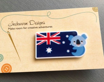 May include: A white plastic button featuring the Australian flag and a cartoon koala bear. The button is labelled with the text "Inchworm Designs" and "Make room for creative adventures".