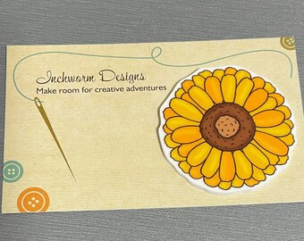 May include: A business card with the text "Inchworm Designs" and the tagline "Make room for creative adventures". A yellow sunflower with a brown center is on the right side of the card.