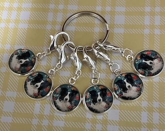 May include: A set of silver-toned keychains with round charms featuring a black and white Border Collie dog portrait surrounded by a floral design. The charms are attached to silver clasps and a keyring.