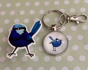 May include: A blue and white bird charm on a silver key ring. The charm is round and has a white background with a blue bird on it. The keyring has a silver ring and a silver clip.