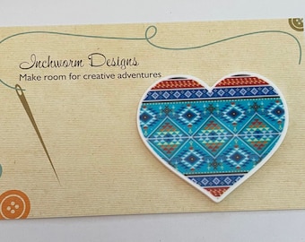 May include: A white heart-shaped pin with a blue, red and yellow geometric pattern. The pin is on a card that says "Inchworm Designs" and "Make room for creative adventures".