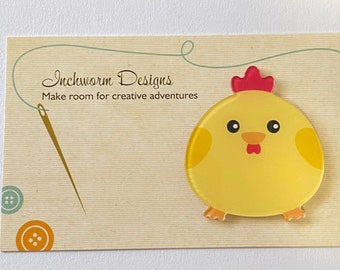 May include: A yellow chick with a red comb and beak, on a card with the text "Inchworm Designs Make room for creative adventures".