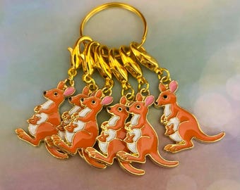 May include: A set of five gold-toned metal stitch markers, each featuring an orange enamel kangaroo charm with a white belly and pink inner ears. Each kangaroo charm includes a small joey in its pouch, attached to a gold lobster clasp ring.