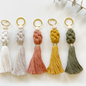 May include: Five keychains with different colored tassels. The tassels are made of woven yarn and have a wooden bead at the top. The keychains are attached to gold metal rings.