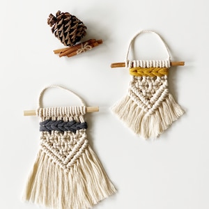 May include: Two small macrame wall hangings with fringe. One has a black and white pattern and the other has a yellow and white pattern.