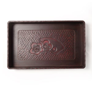 May include: A rectangular dark brown wooden tray featuring a carved central panel with a textured honeycomb pattern. The design includes a relief carving of two plum blossoms and a folding fan motif, with subtle red highlights in the grooves.