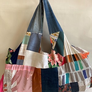 Può includere: Una grande borsa tote patchwork con cinturini in denim e una varietà di toppe in tessuto. La borsa presenta tessuti floreali, a righe e tinta unita nei toni del blu, rosa e verde. La borsa è progettata con una grande capacità.