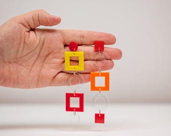 May include: A pair of colorful geometric earrings with red, yellow, and orange squares and circles hanging from silver chains.