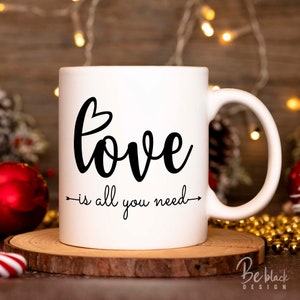 May include: White ceramic mug with black text that reads "love is all you need" with a small heart above the word "love".