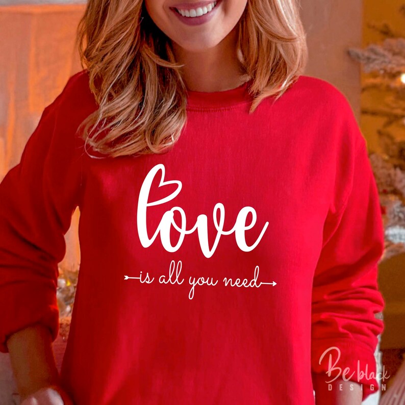 May include: Red sweatshirt with white text that reads "love is all you need" with an arrow pointing to the left and right of the text.