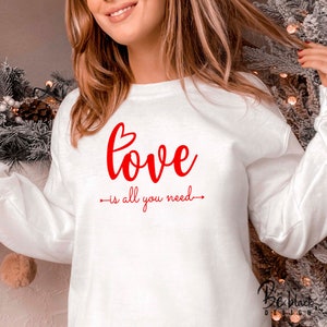 May include: White sweatshirt with red text that reads "love is all you need" with a heart symbol above the word "love".