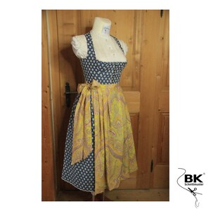 Peut inclure: Une robe traditionnelle bavaroise bleue et jaune avec un chemisier blanc et une ceinture jaune. La robe est orn&eacute;e d'une dentelle blanche et d'un motif floral.