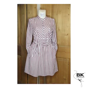 Puede incluir: Un vestido de rayas blancas y burdeos con manga larga, cierre de botones y cinturón de lazo. El vestido tiene un escote en V y bolsillos en los laterales.