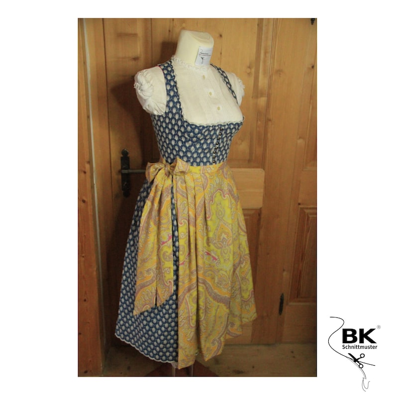 Peut inclure: Une robe traditionnelle bavaroise &agrave; pois bleus et blancs avec un tablier &agrave; imprim&eacute; paisley jaune et rose. La robe est accompagn&eacute;e d'un chemisier blanc &agrave; col en dentelle.
