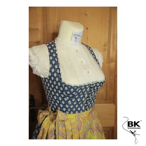 Peut inclure: Une robe traditionnelle bavaroise bleue et blanche avec une jupe jaune &agrave; imprim&eacute; paisley. Le corsage est orn&eacute; d'une dentelle blanche et d'une rang&eacute;e de boutons sur le devant. La jupe est agr&eacute;ment&eacute;e d'un n&oelig;ud jaune &agrave; la taille.