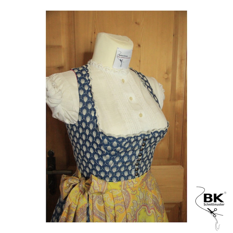 Peut inclure: Une robe traditionnelle bavaroise bleue et blanche avec une jupe jaune &agrave; imprim&eacute; paisley. Le corsage est orn&eacute; d'une dentelle blanche et d'une rang&eacute;e de boutons sur le devant. La jupe est agr&eacute;ment&eacute;e d'un n&oelig;ud jaune &agrave; la taille.