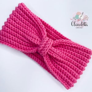 Könnte beinhalten: Ein handgehäkeltes Stirnband in leuchtendem Pink. Das Stirnband hat eine gerippte Textur und ein geknotetes Detail in der Mitte. Das Claudetta Crochet-Logo ist sichtbar. Dieses Accessoire ist ideal, um jedem Outfit einen Farbtupfer zu verleihen.