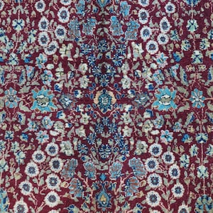 May include: A close-up of a red rug with a floral pattern. The rug features a variety of blue, white, and green flowers.