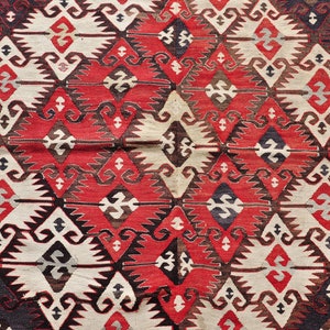 May include: A close-up of a traditional Turkish rug with a geometric pattern in shades of red, white, black, and brown.