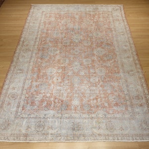May include: A vintage rug with a faded floral pattern in shades of pink, white, and blue. The rug has a border with a repeating geometric design.