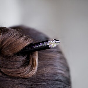 May include: A black hair stick with a clear crystal tip containing pressed purple flowers.