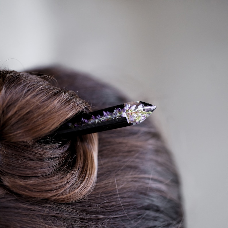 May include: A black hair stick with a clear crystal tip containing pressed purple flowers.