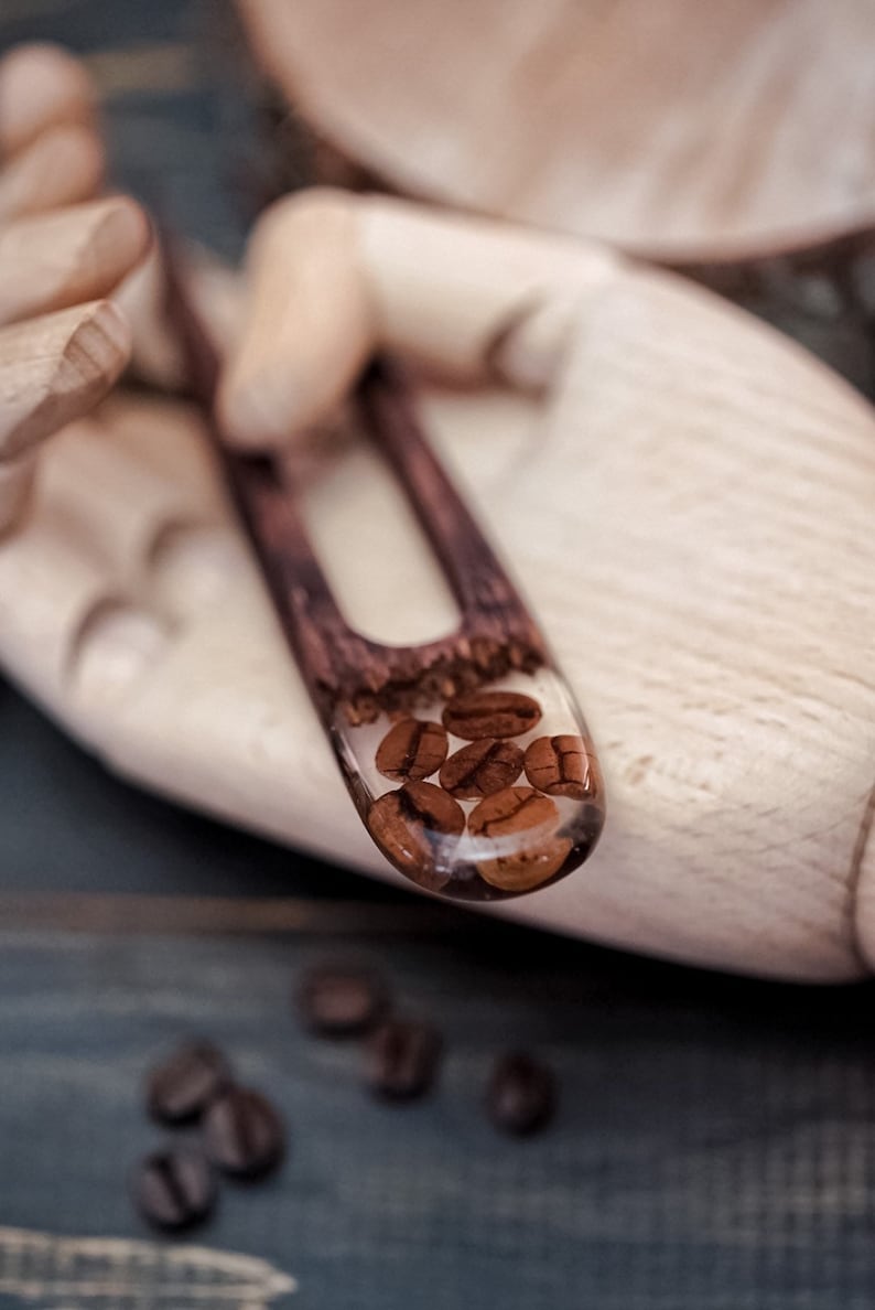 May include: A wooden hair comb with a clear resin section filled with coffee beans. The comb is held in a wooden hand.