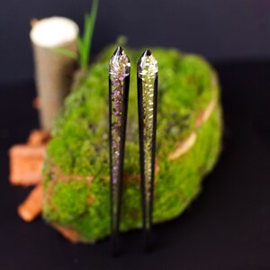 May include: Two clear resin hair sticks with a pointed top. One stick features a purple flower design and the other a white flower design.