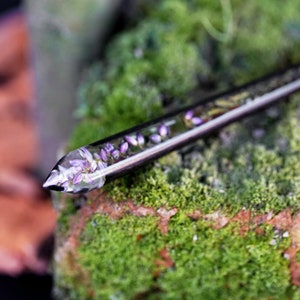 May include: A clear glass rod with a silver metal cap, filled with small purple flowers. The rod is resting on a bed of green moss.