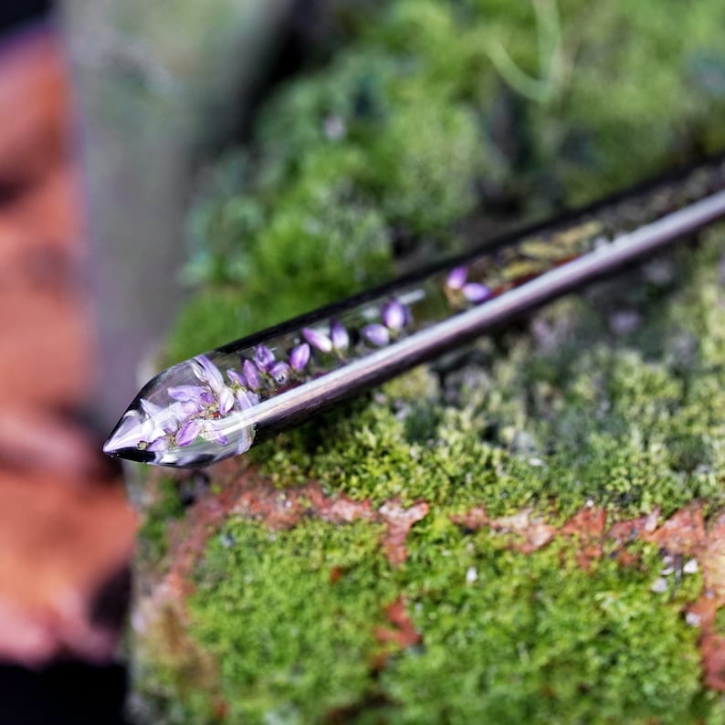 May include: A clear glass rod with a silver metal cap, filled with small purple flowers. The rod is resting on a bed of green moss.