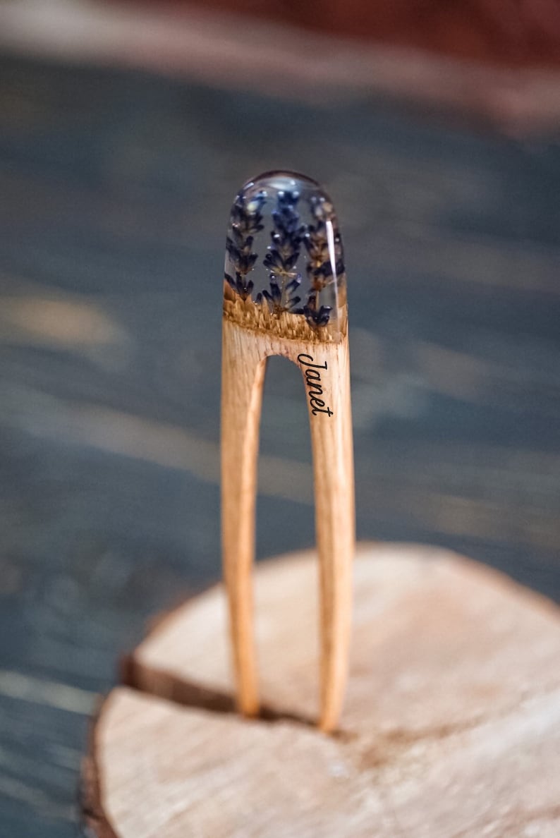 May include: A wooden hair stick with a clear resin top containing dried lavender flowers. The stick is engraved with the name "Janet".