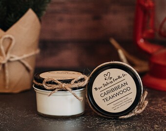 May include: Two small glass jars with lids. The jars are filled with white wax and have brown twine tied around the lids. The jar on the right has a brown paper label with the text "Three Sisters Candle Co. CARIBBEAN TEAKWOOD Scented Soy Candle Hand Poured in Tennessee Net Wt. 2.75 oz (77.9 g)"