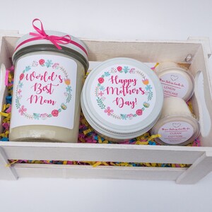 Op de afbeelding: Een witte houten kist gevuld met kleurrijk versnipperd papier en drie kaarsen. De kaarsen zitten in glazen potten met etiketten waarop staat "World's Best Mom", "Happy Mother's Day!" en "Lemon Cupcake" en "Clean Cotton".