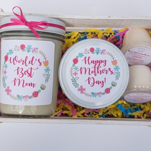 Op de afbeelding: Een witte houten doos gevuld met kleurrijk tissuepapier en een kaars met een bloemmotief en de tekst "World's Best Mom". Er is ook een kaars met een bloemmotief en de tekst "Happy Mother's Day!" en twee kleine kaarsen met de tekst "Lemon Poundcake".