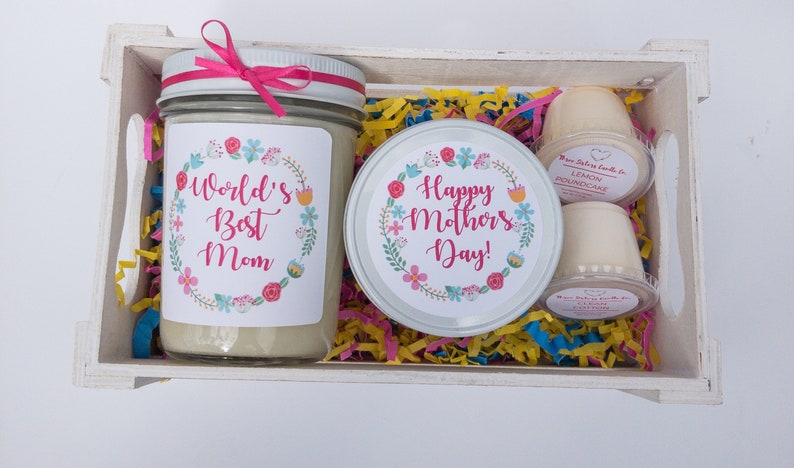 Op de afbeelding: Een witte houten doos gevuld met kleurrijk tissuepapier en een kaars met een bloemmotief en de tekst "World's Best Mom". Er is ook een kaars met een bloemmotief en de tekst "Happy Mother's Day!" en twee kleine kaarsen met de tekst "Lemon Poundcake".