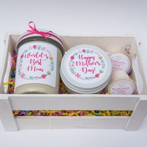 Op de afbeelding: Een witte houten kist gevuld met kleurrijk tissuepapier en drie kaarsen. De kaarsen zitten in glazen potten met etiketten waarop staat "World's Best Mom", "Happy Mother's Day!" en "Lemon Poundcake" en "Clean Cotton".