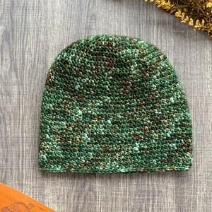 May include: A green and brown crocheted beanie hat with a camouflage pattern.