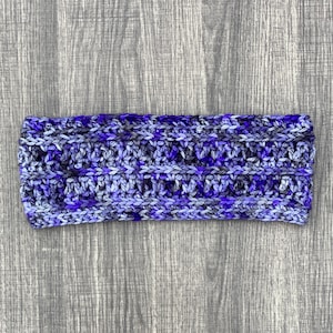Puede incluir: Una diadema de crochet de color morado y blanco con un patrón texturizado.