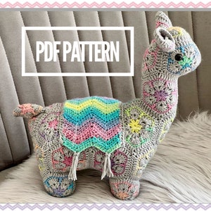 Op de afbeelding: Een gehaakt lama amigurumi speelgoed met een kleurrijk gestreept deken. De lama is grijs met een veelkleurig geometrisch patroon. De tekst "PDF PATTERN" wordt weergegeven op een wit rechthoek.