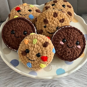 May include: Five crocheted cookies with smiling faces on a white plate with blue and brown polka dots. The cookies are brown, tan, and a mix of brown and colourful sprinkles. The plate has the text "stitch & stuff" on it.