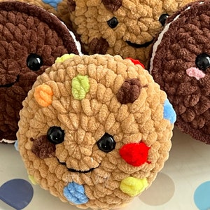 May include: A collection of crocheted cookies with colourful sprinkles and smiling faces. The cookies are brown, tan, and white.