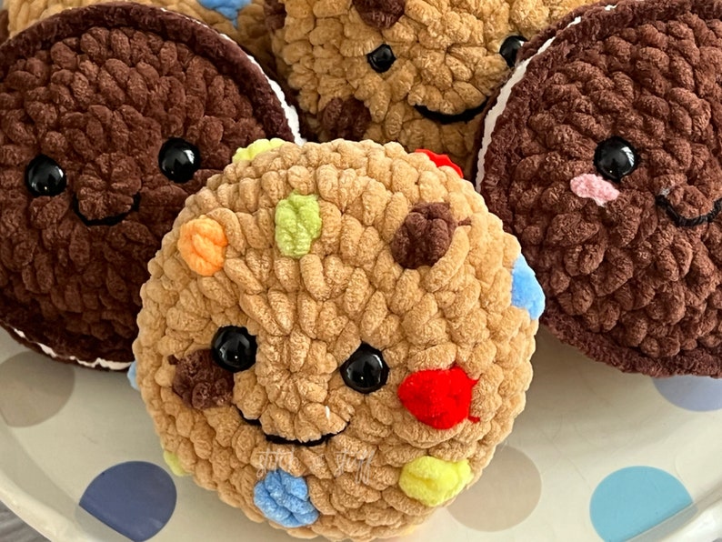 May include: A collection of crocheted cookies with colourful sprinkles and smiling faces. The cookies are brown, tan, and white.