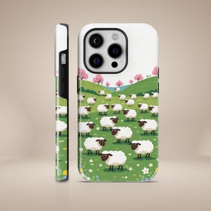 May include: A white iPhone case with a black camera lens and a design of a green field with white sheep and pink flowers.