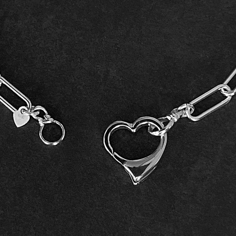 May include: A silver chain bracelet with a heart-shaped clasp. The chain is made of oval links.