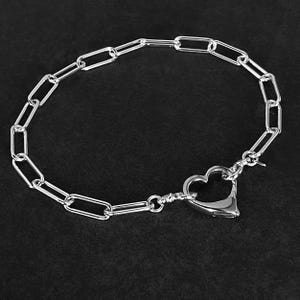 May include: A silver chain necklace with a heart-shaped clasp. The chain is made of oval links.