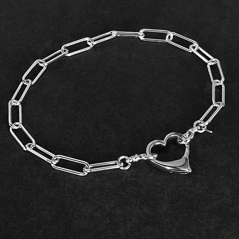 May include: A silver chain necklace with a heart-shaped clasp. The chain is made of oval links.