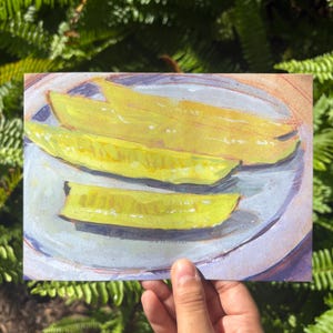 Puede incluir: Una impresión artística rectangular que muestra una pintura de tres pepinillos de color amarillo brillante dispuestos sobre un plato azul claro. La obra utiliza pinceladas visibles y una paleta de colores amarillo, azul claro y violeta.