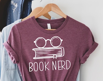 May include: A maroon t-shirt with a white graphic of a book with glasses on top and the text "BOOK NERD".