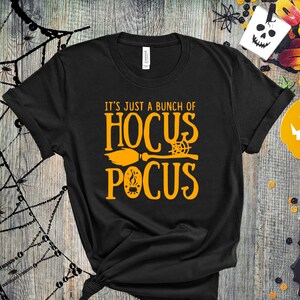 May include: Black t-shirt with the text "It's just a bunch of Hocus Pocus" in orange. A broom and a spiderweb are included in the design.