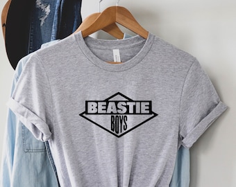 May include: A gray t-shirt with a black diamond-shaped logo that says "BEASTIE BOYS" in all caps.